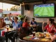 Fans enjoying كورة لايف match with drinks, snacks, and team flags at outdoor café source.